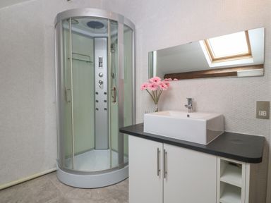 A bathroom with a corner glass shower unit and a sink with a black countertop and a mirror at Apartment 2 Gorwel Glas in Llanbedrog