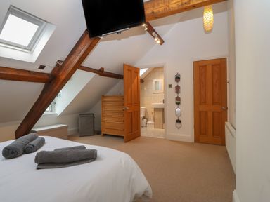 A bedroom with bed and towels a wooden chest of drawers a skylight and an en suite bathroom at Apartment 2 Gorwel Glas in Llanbedrog