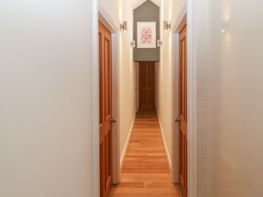 A narrow hallway with wooden doors on both sides and a framed picture at the end at Apartment 2 Gorwel Glas Llanbedrog