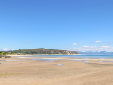A sandy beach with shallow water pools and hills in the background at Apartment 2 Gorwel Glas in Llanbedrog