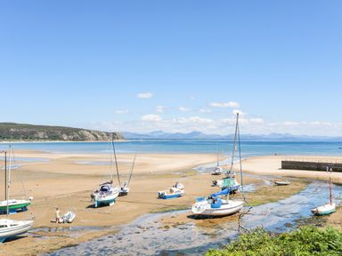 Boats resting on a sandy shore during low tide with a view of the sea and hills at Apartment 2 Gorwel Glas in Llanbedrog