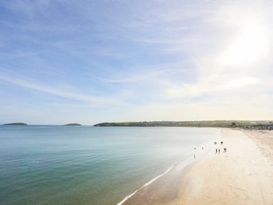 A beach with calm water and people walking near the shore at Apartment 2 Gorwel Glas in Llanbedrog