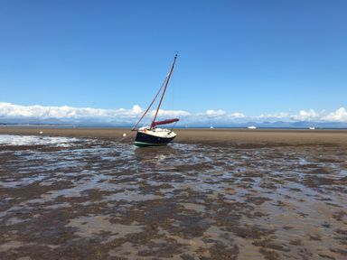 A sailboat grounded on a tidal flat with other boats in the distance at Apartment 2, Gorwel Glas in Llanbedrog