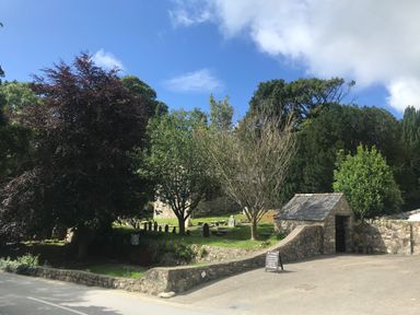 A small stone building and trees surrounding a churchyard with gravestones at Apartment 2 Gorwel Glas in Llanbedrog