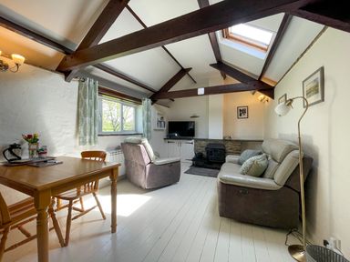 A living room with wood beams a table two chairs two armchairs a television and a fireplace at The Stable @ Canllefaes Penparc near Cardigan