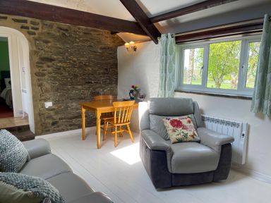 A living room with a gray armchair and wooden table near a stone wall and window at The Stable @ Canllefaes in Penparc near Cardigan