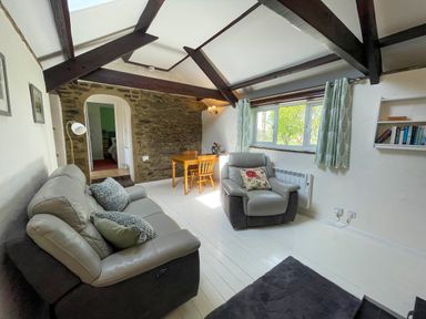 A living room with gray sofas a wooden table and chairs and a window with curtains at The Stable @ Canllefaes in Penparc near Cardigan