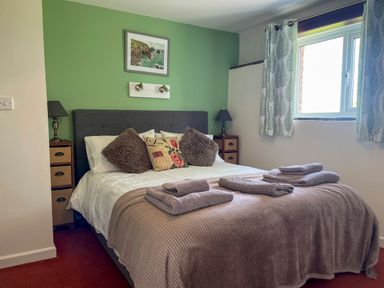 A bedroom with a double bed, bedside tables with lamps, framed artwork, and window curtains at The Stable @ Canllefaes in Penparc near Cardigan