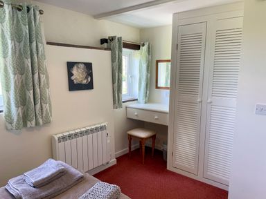 A bedroom corner with a window, a dressing table with mirror, a stool, a wardrobe, and a bed with folded towels at The Stable @ Canllefaes Penparc near Cardigan