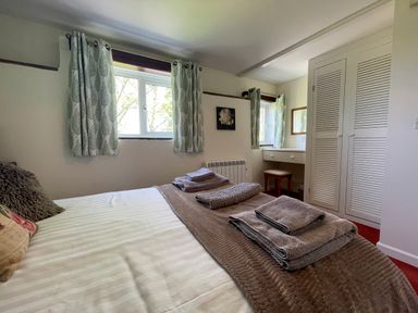 A bedroom with a bed and folded towels on it next to windows with curtains and a vanity area at The Stable @ Canllefaes in Penparc near Cardigan