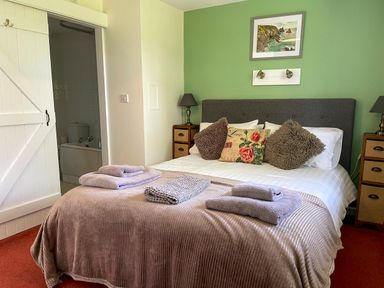 A bedroom with a bed made up with pillows and towels with an open door leading to a bathroom at The Stable at Canllefaes Penparc near Cardigan