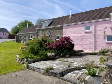 A stone and pink painted house with a garden and paved patio at The Stable @ Canllefaes in Penparc near Cardigan