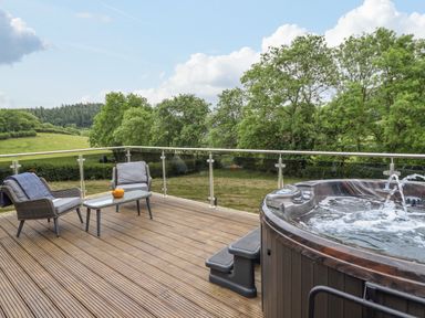 An outdoor deck with two chairs a table and a hot tub overlooking trees and fields at The Cabin at Evelyns Retreat in Glyndyfrdwy
