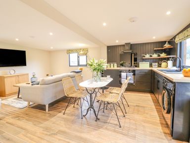 An open living room and kitchen with a sofa a dining table with four chairs and kitchen appliances at The Cabin at Evelyns Retreat in Glyndyfrdwy