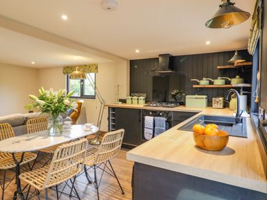 A kitchen and dining area with a wooden table and wicker chairs at The Cabin at Evelyns Retreat in Glyndyfrdwy