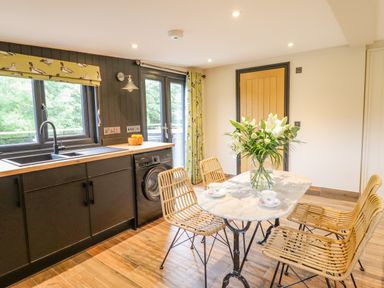 A kitchen with black cabinets a washing machine a marble table with chairs and flowers at The Cabin at Evelyns Retreat in Glyndyfrdwy