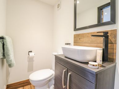 A bathroom with a toilet a sink on a cabinet a mirror a towel on a rack and toiletries at The Cabin at Evelyns Retreat in Glyndyfrdwy