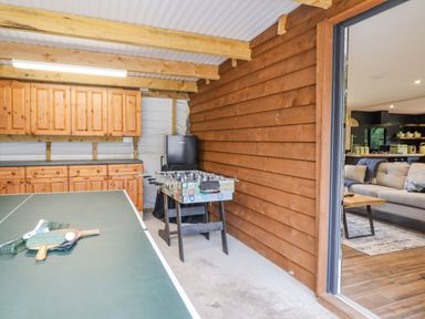 A game room with a ping pong table foosball table wooden cabinets and a view into a living room at The Cabin at Evelyns Retreat in Glyndyfrdwy
