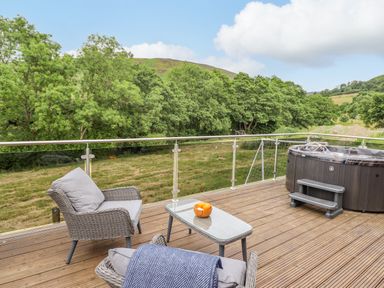 An outdoor deck with two armchairs a glass table with a bowl of oranges and a hot tub overlooking a grassy area at The Cabin at Evelyns Retreat in Glyndyfrdwy