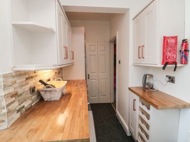 A galley kitchen with wooden countertops white cabinets a basket with a bottle a kettle a fire blanket and a fire extinguisher at The Wizard's Loft in Alnwick