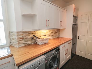 A kitchen with wooden countertop washing machine fridge and white cabinets at The Wizard's Loft in Alnwick