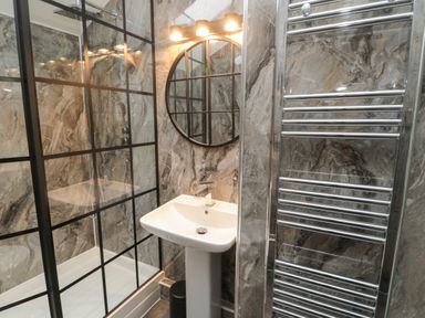 A bathroom with a pedestal sink a round mirror and a shower enclosure with a black grid frame at The Wizard's Loft in Alnwick
