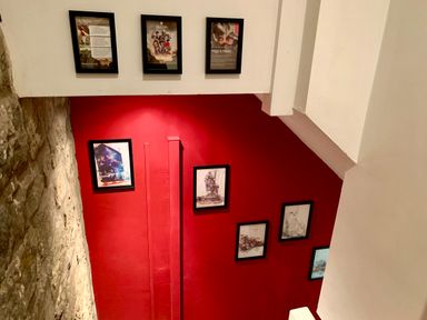 A staircase wall painted red with framed pictures and a stone wall on the left at The Wizard's Loft in Alnwick