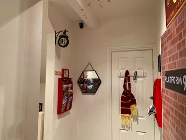 A hallway with a Platform 9 3 4 sign a hexagonal mirror a red and yellow scarf hanging on a door and red brochure holders at The Wizards Loft in Alnwick