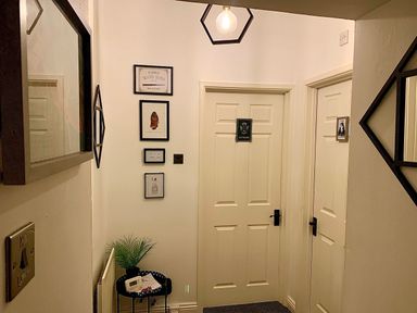 A hallway with three closed doors two mirrors pictures and a small table with a plant and thermometer at The Wizard's Loft in Alnwick