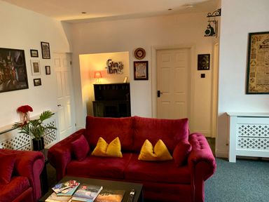 A living room with red sofas yellow cushions framed pictures a table with books and a lamp at The Wizards Loft in Alnwick