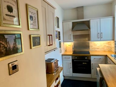 A kitchen with white cabinets wooden countertops a copper toaster and framed pictures on the wall at The Wizards Loft in Alnwick