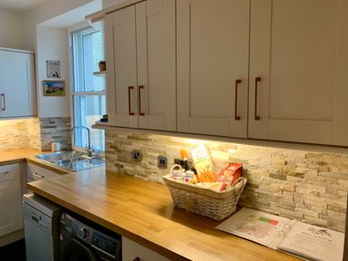 A kitchen with wooden countertop cabinets a basket of snacks a window and a sink at The Wizards Loft in Alnwick