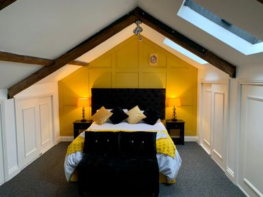 A bedroom with a double bed yellow wall panels black headboard and pillows two bedside tables with lamps under wooden beam skylights at The Wizard's Loft in Alnwick