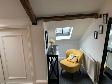 A small corner with a yellow chair and a black console table under a skylight window at The Wizard's Loft in Alnwick