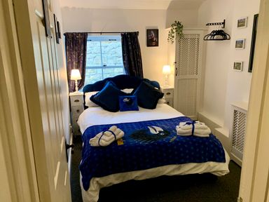 A bedroom with a bed, blue pillows, bedside tables with lamps, a wardrobe, and a window with curtains at The Wizard's Loft in Alnwick