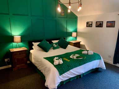 A bedroom with a large bed with green and white bedding two bedside tables with lamps and framed pictures on the wall at The Wizards Loft in Alnwick