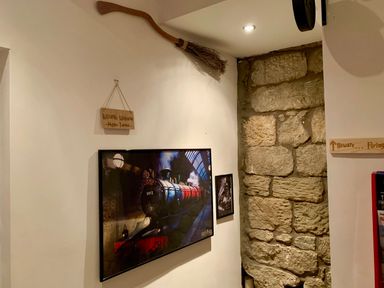 A wall with a broomstick hanging above framed pictures and a wooden sign in a room with exposed stone at The Wizard's Loft in Alnwick