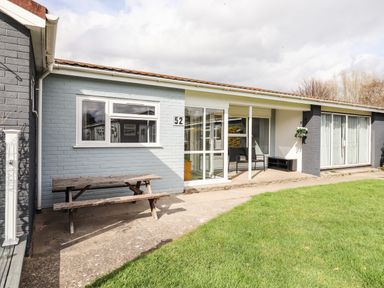 Exterior of a single-story house with a wooden picnic table and green lawn at Marsh Bungalow in Lowestoft