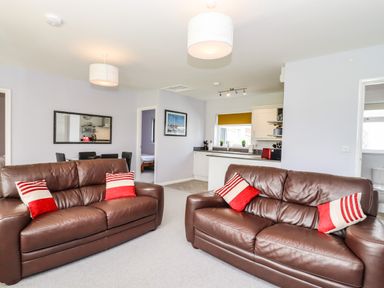 A living room with two brown leather sofas with red and white pillows an open kitchen and a dining area at Marsh Bungalow in Lowestoft