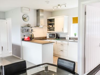 A kitchen with white cabinets a red toaster a microwave and a glass dining table with black chairs at Marsh Bungalow in Lowestoft