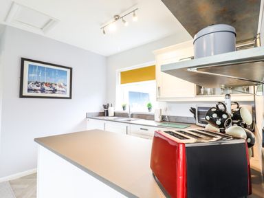 A kitchen with a countertop a red toaster mugs on a rack a picture on the wall and a window with a yellow blind at Marsh Bungalow in Lowestoft