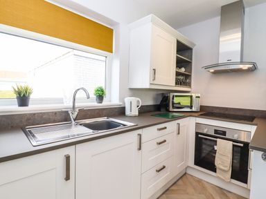 A kitchen with a stainless steel sink microwave oven kettle and white cabinets at Marsh Bungalow in Lowestoft