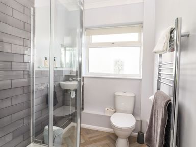 A bathroom with a shower enclosure a toilet a small sink a window and a heated towel rail at Marsh Bungalow in Lowestoft
