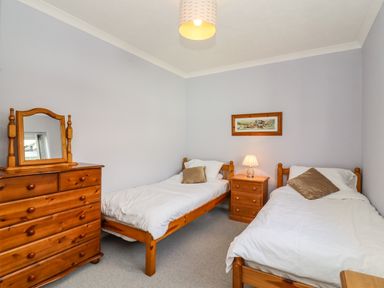 A bedroom with two single beds a wooden dresser and a bedside table with a lamp at Marsh Bungalow in Lowestoft