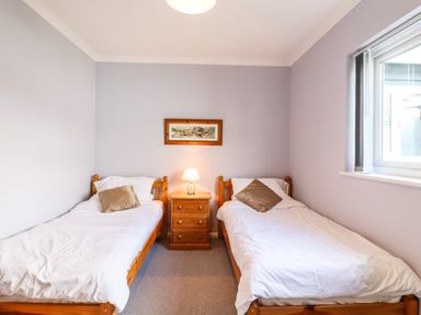 A bedroom with two single beds a nightstand with a lamp and a window at Marsh Bungalow in Lowestoft