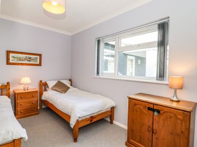 A bedroom with two single wooden beds wooden furniture and a window at Marsh Bungalow Lowestoft