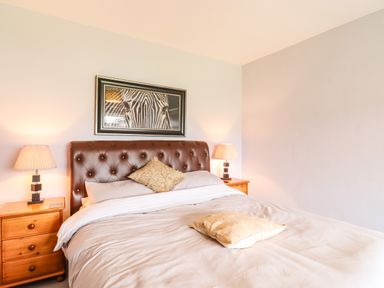 A bedroom with a double bed two bedside tables with lamps and a zebra picture on the wall at Marsh Bungalow in Lowestoft