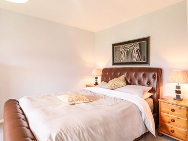 A bedroom with a brown leather bed frame two bedside tables with lamps and a zebra picture on the wall at Marsh Bungalow in Lowestoft