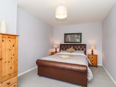 A bedroom with a brown leather bed a wooden wardrobe and two bedside tables with lamps at Marsh Bungalow in Lowestoft