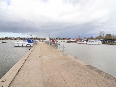 A concrete dock with boats moored on both sides of a river under a cloudy sky